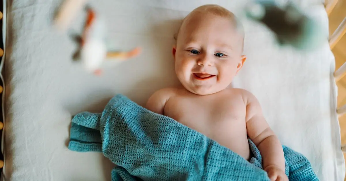 Swaddling and baby sleep concept featuring a smiling baby lying in a crib with a soft blanket, demonstrating a calm and comfortable sleep environment for newborns.