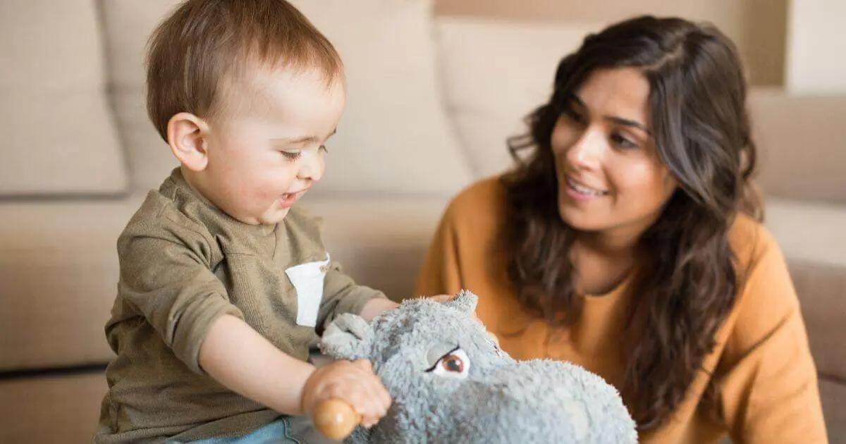 What to Play With Your Baby (3–12 Months): Simple Developmental Activities What to Play With Your Baby: mom helping baby boy play on a rocking horse at home.