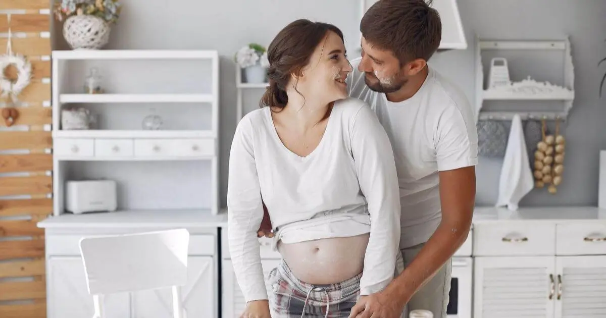 Becoming a parent isn’t a single moment — so when does it actually begin? Becoming a parent moment showing a loving couple embracing in the kitchen while expecting their baby.