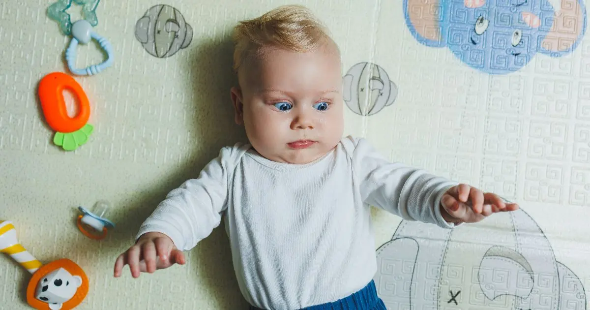 High needs baby lying on a play mat with an intense facial expression, showing alertness, sensitivity, and constant stimulation needs during infancy.