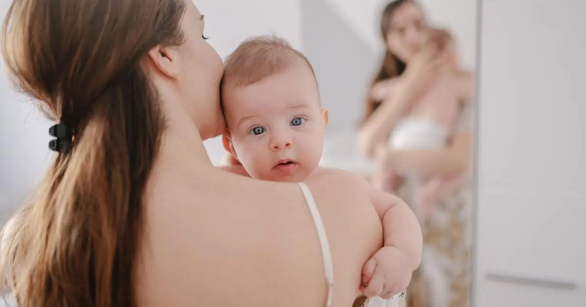 Postpartum Recovery after childbirth as a new mother holds her baby in front of a mirror, embracing her changing body and the emotional journey of healing.