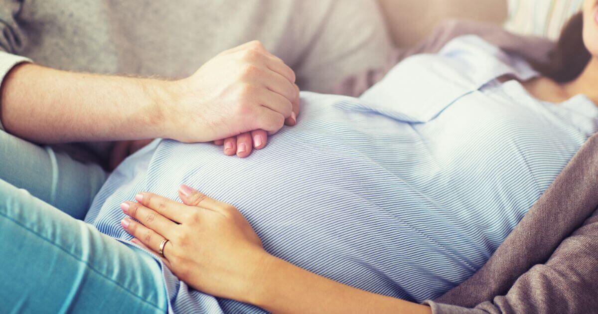 Close-up of a man gently touching a pregnant woman’s belly, representing early fatherhood and the emotional connection during pregnancy.