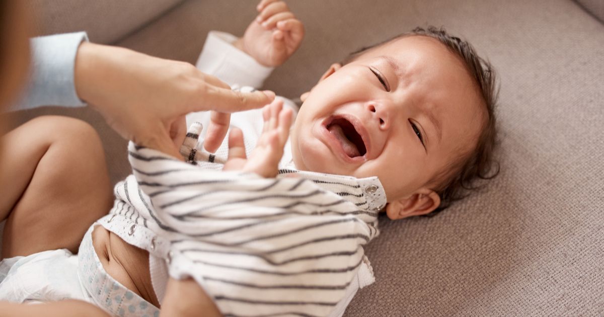 Soothing a baby: a crying baby lying on a couch while a parent gently tries to comfort and calm them during a diaper or clothing change.