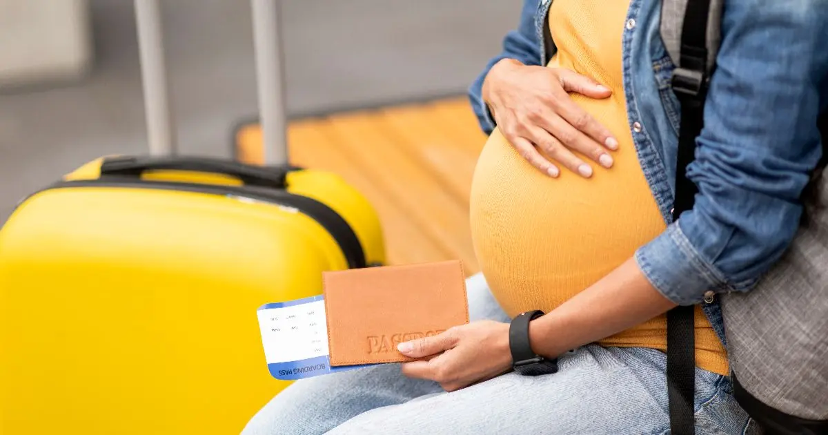 Traveling While Pregnant woman sitting with suitcase and passport ready for a safe journey