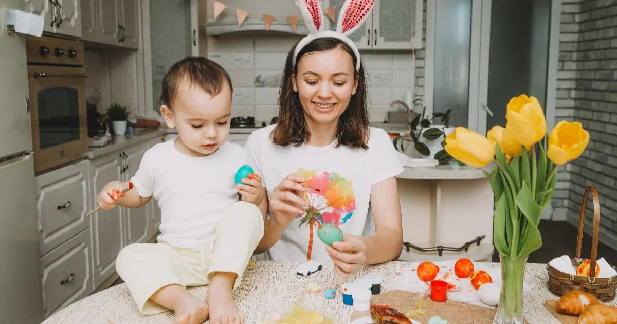 mother and child painting easter eggs together in kitchen during easter preparation