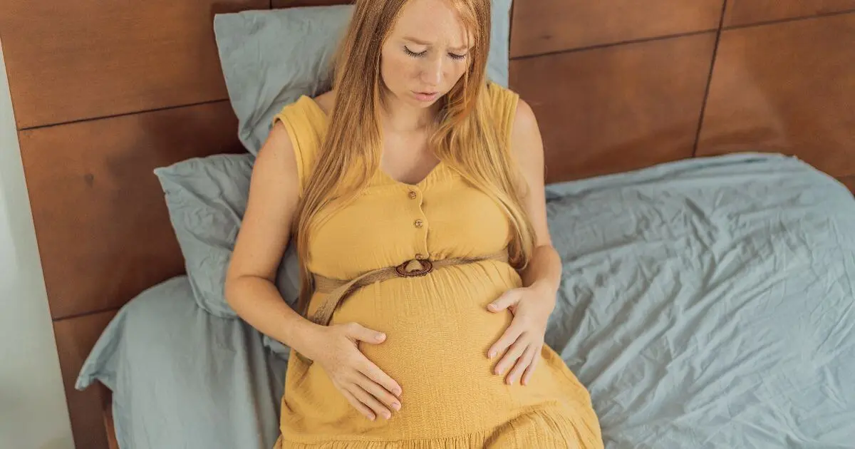 Pregnant woman sitting on a bed while experiencing discomfort and possible labor contractions during the final weeks of pregnancy.