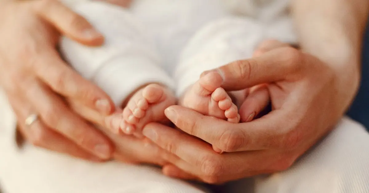 Baby Visitors gently holding newborn baby feet in close-up moment