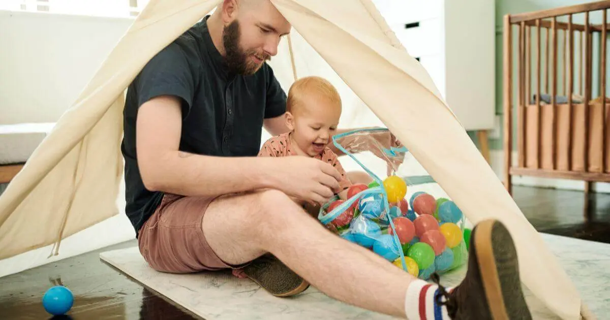 What to Play With Your Baby (3–12 Months): Simple Developmental Activities What to Play With Your Baby: father and baby boy playing with colorful balls in bedroom play tent
