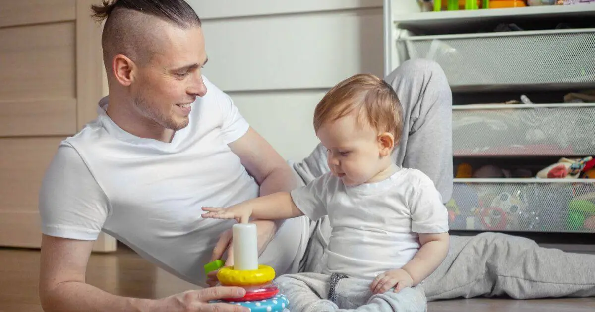 What to Play With Your Baby (3–12 Months): Simple Developmental Activities What to Play With Your Baby: father and baby son playing with a stacking pyramid toy in the nursery