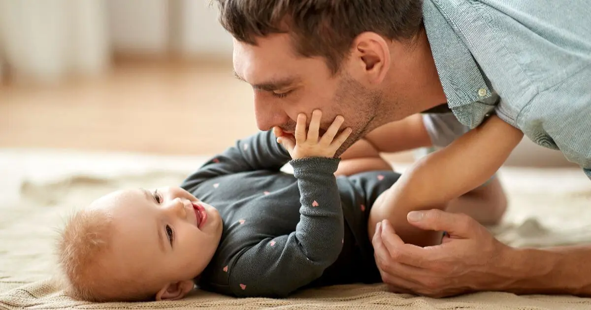 The Simplest Way to Become the Father Your Child Will Never Forget Father gently playing with his smiling baby on the floor, showing loving bonding moments and emotional connection during everyday baby care at home.