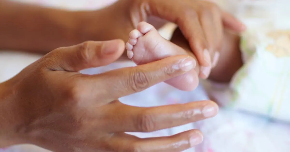 Newborn Care: close-up of baby feet while mother gently soothes and cares for her newborn