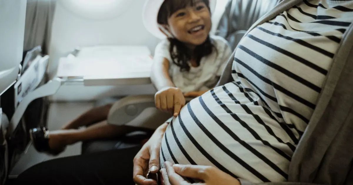Traveling While Pregnant on a plane with child touching baby bump during a calm flight moment