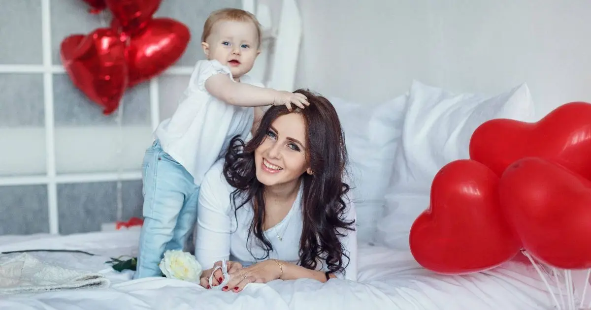 Happy mother and young daughter sharing a loving hug and kiss at home, capturing a warm family moment during Valentine’s Day with a baby.