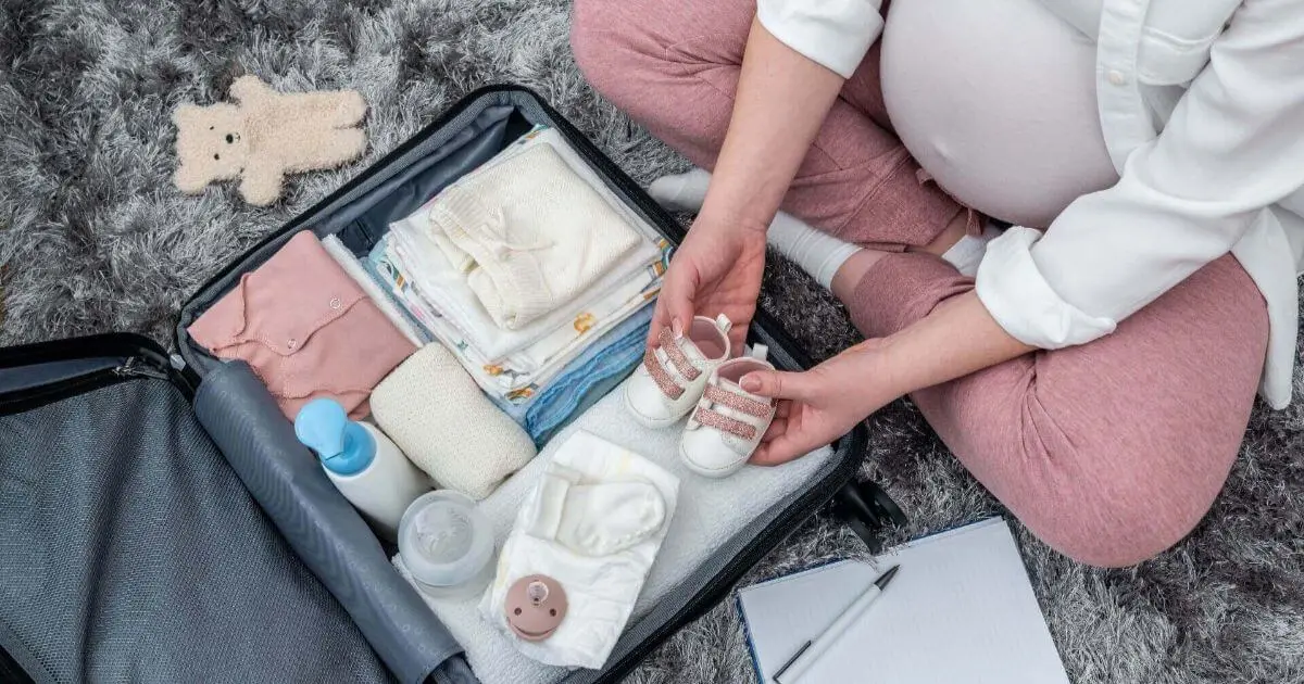 Pregnant woman packing baby essentials and tiny shoes into a suitcase, featuring a practical Hospital Bag Checklist for labor, delivery, and the baby’s first days.