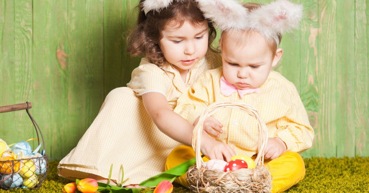 two little kids dressed as bunnies playing with eggs on grass during easter preparation