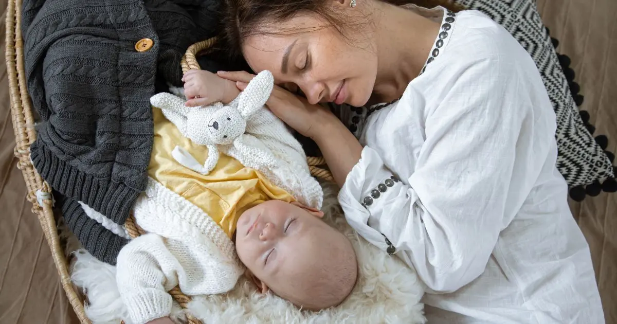 Matrescence: Exhausted mother sleeping next to her peacefully resting baby in a Moses basket, symbolizing the fatigue, love, and transformation of matrescence.