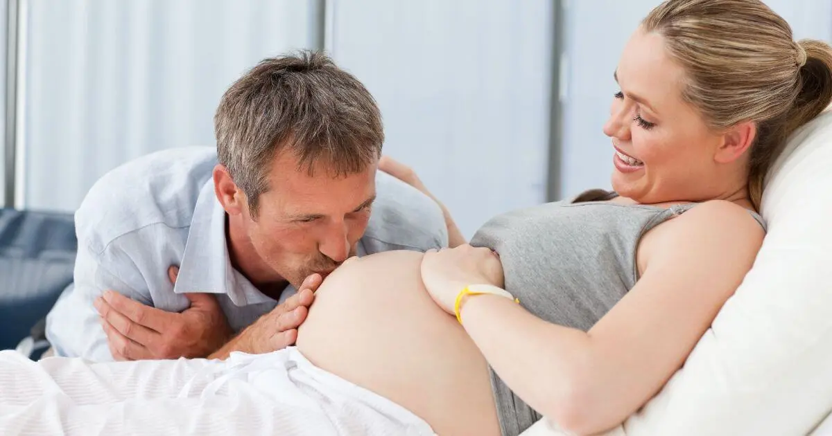 Becoming a parent isn’t a single moment — so when does it actually begin? Expectant father kissing his pregnant wife’s belly at home while they discuss their home birth or hospital birth decision in a calm, intimate setting.