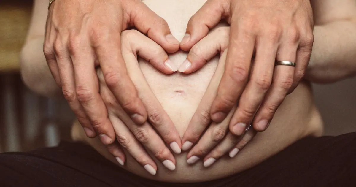 A man and a woman holding hands on a pregnant belly, symbolizing partner-supported birth and emotional support during pregnancy.