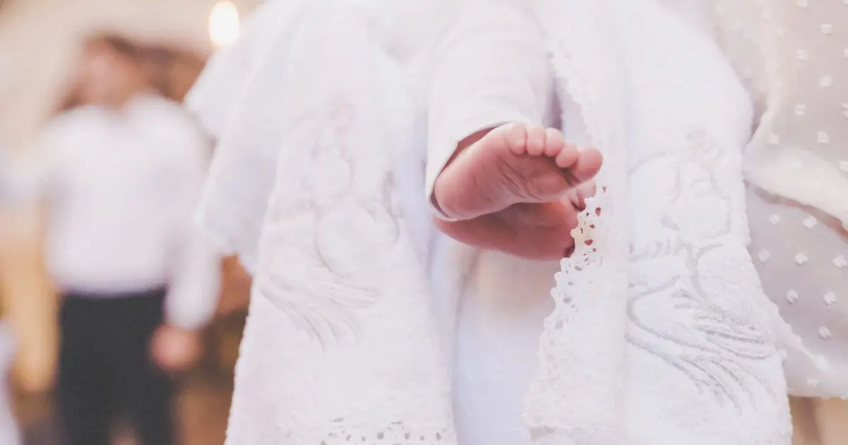 Close-up of baby in white outfit during Baptism, held gently by mother
