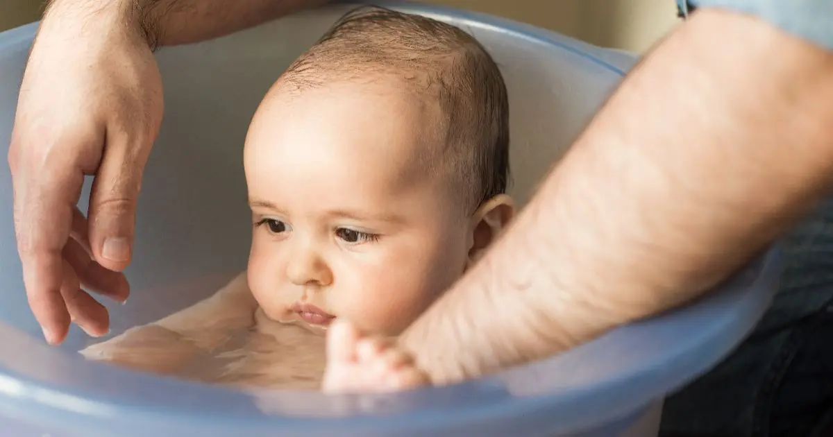 Father giving a gentle baby bath to his newborn baby as part of a safe and soothing baby care routine.