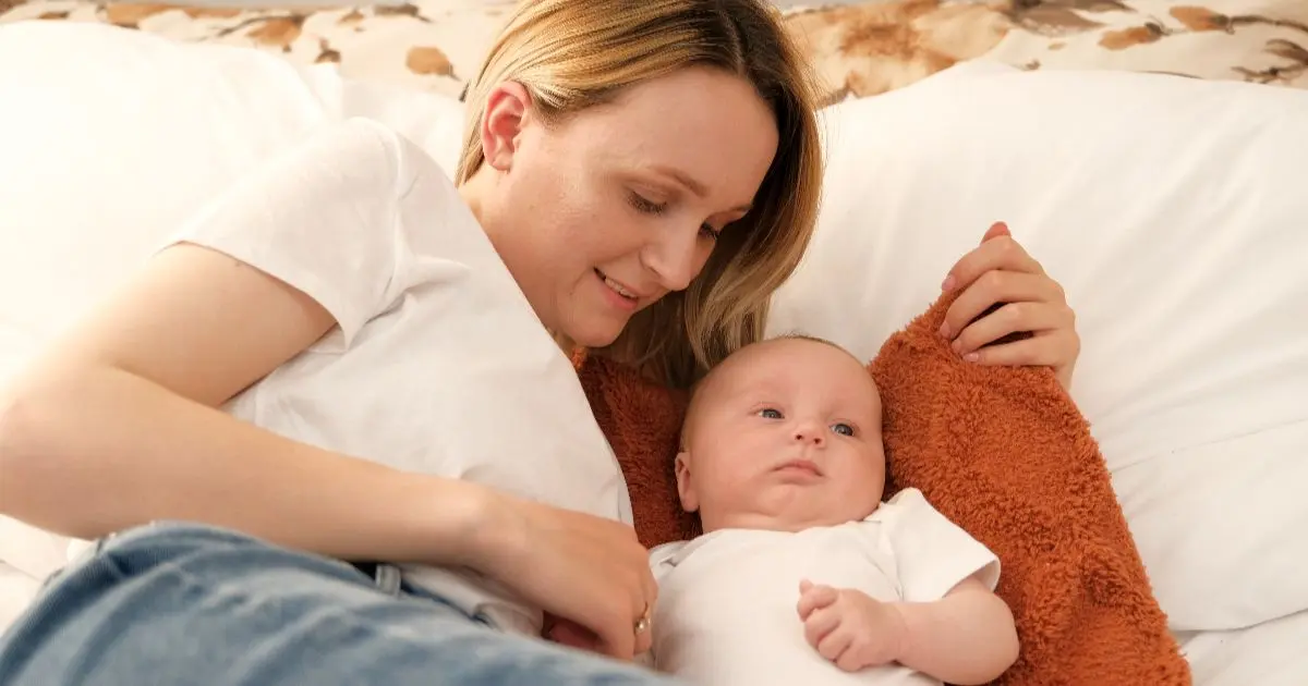 Matrescence: Mother relaxing beside her awake baby in bed, reflecting the everyday emotional and physical changes that come with matrescence and new motherhood.