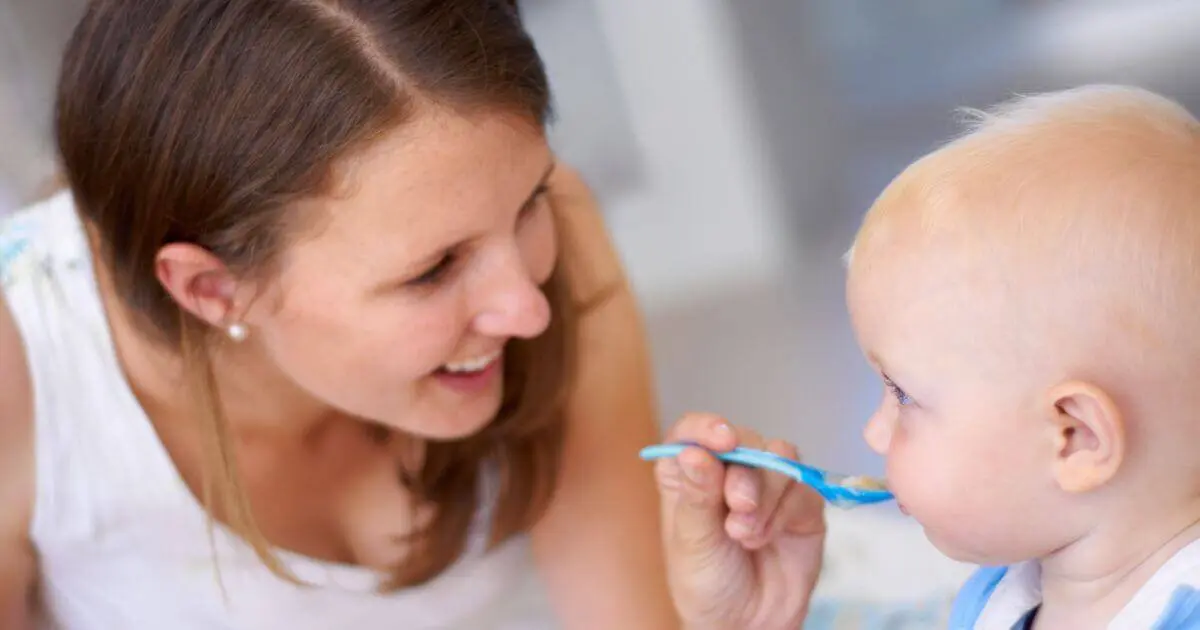 Introducing Solids Step by Step: What, When, and How to Feed Your Baby Mother introducing solids to her baby with a spoon during breakfast at home, supporting healthy growth and development.