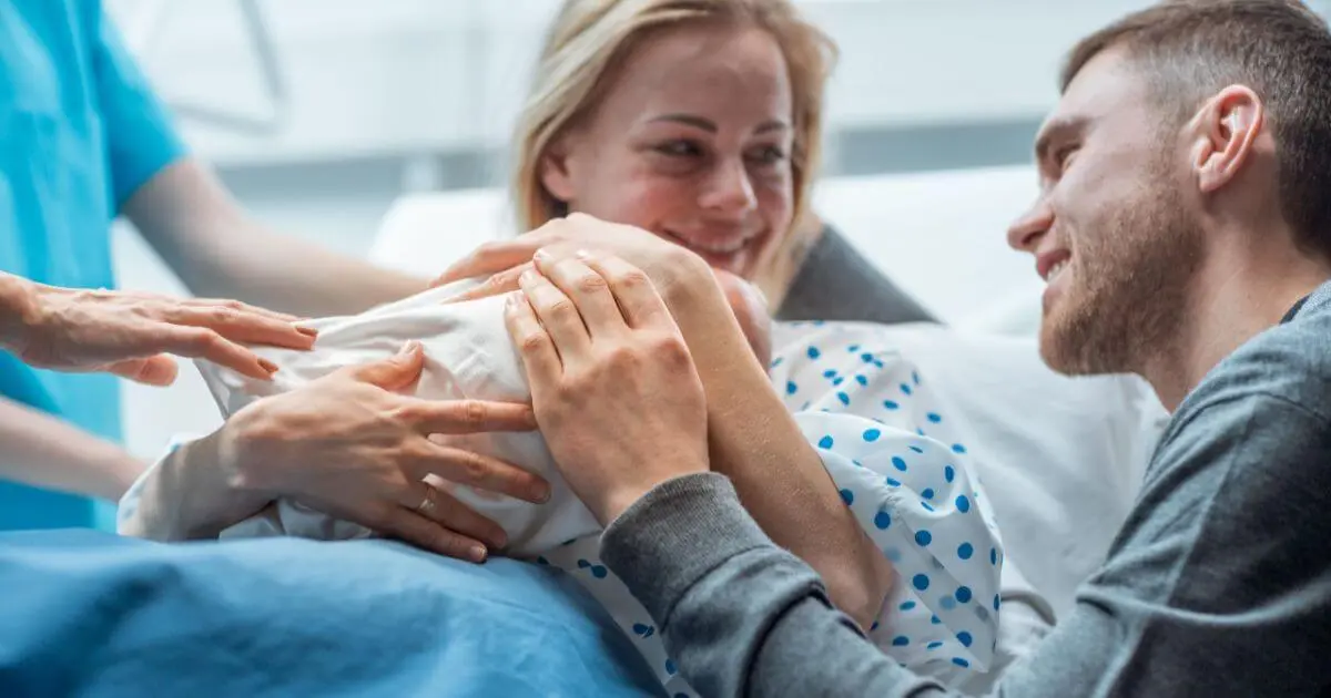 A smiling mother holding her baby while looking at the camera, capturing a warm family moment connected to early fatherhood and parenthood.