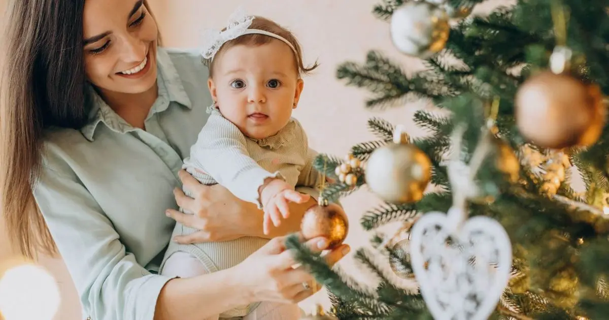 Your Baby’s First Christmas – Small Moments, First Memories Mother with her baby daughter decorating a Christmas tree together, creating warm holiday moments during baby’s first Christmas