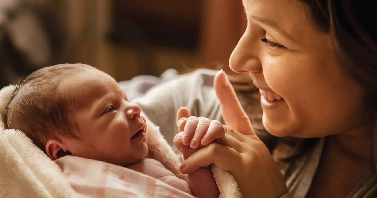 Matrescence: Mother smiling lovingly at her newborn as they make eye contact, capturing the emotional bond and identity transformation of early motherhood.