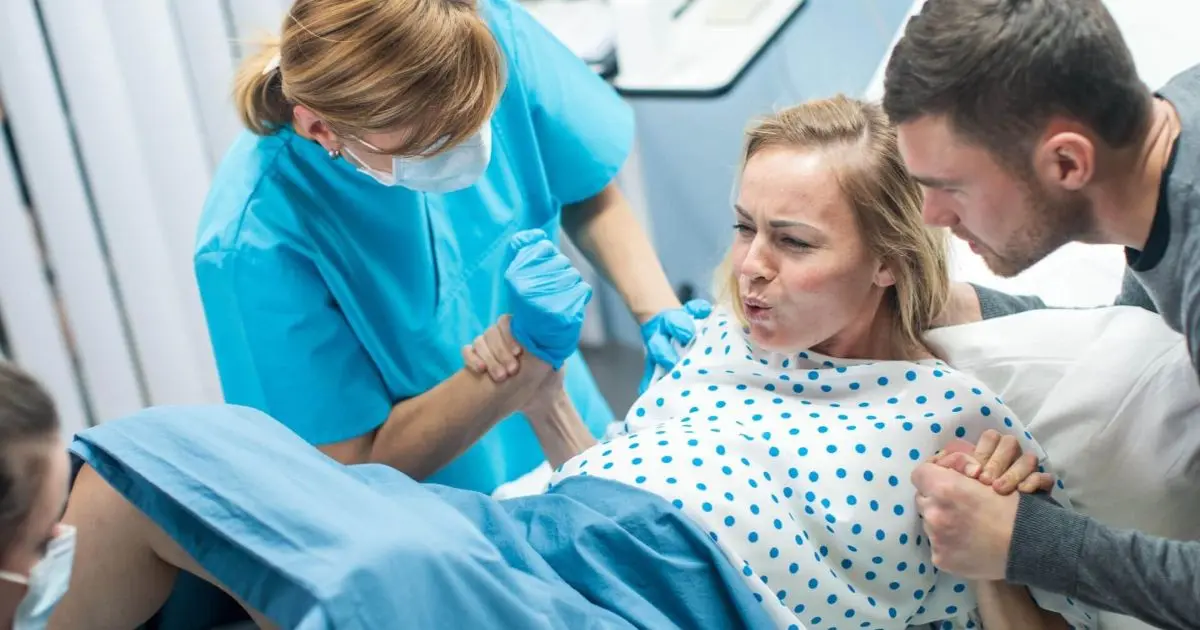 Partner-Supported Birth – A Shared Experience or Too Much Pressure? Nurse helping a mother in a hospital bed after delivery, reflecting birth trauma and emotional recovery following a difficult birth experience.
