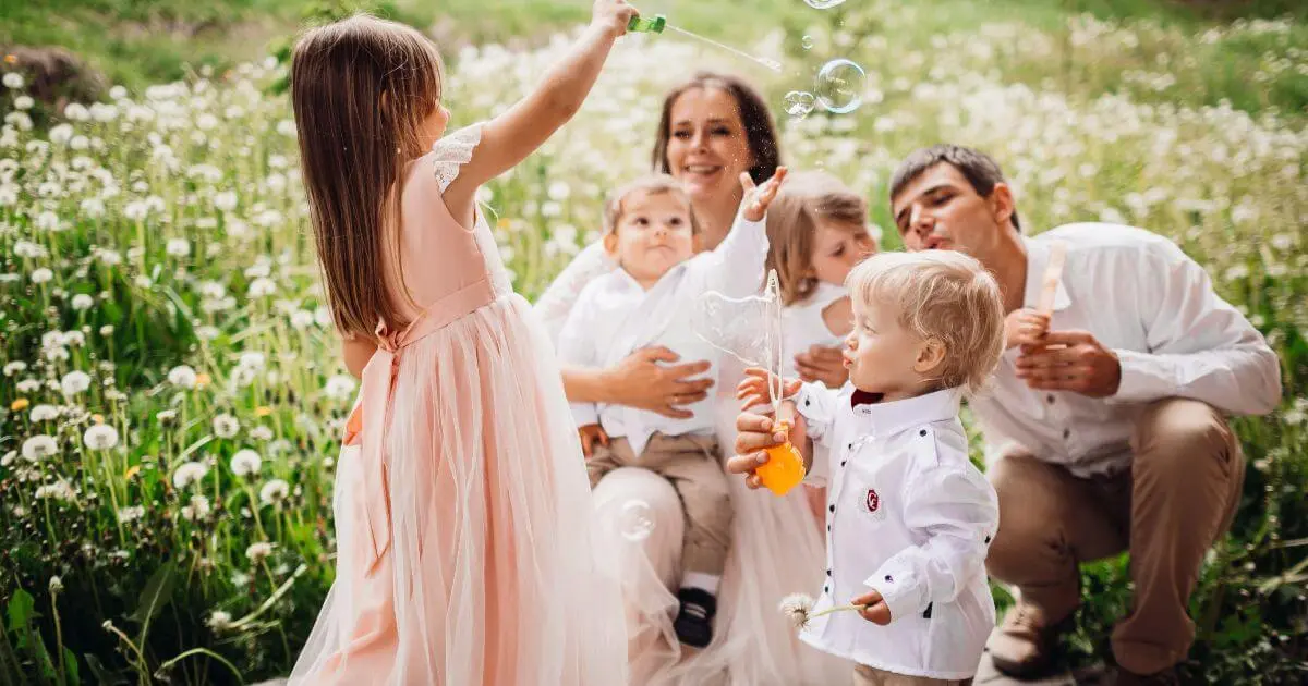 Family celebrating Baptism day outdoors, children playing bubbles in a happy atmosphere