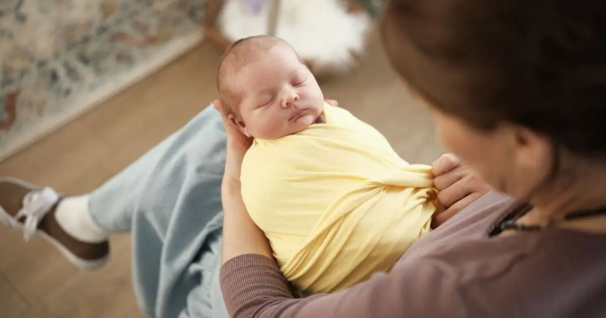Mother holding a swaddled newborn wrapped in a soft blanket, illustrating the benefits of swaddling for comfort, security, and better baby sleep.