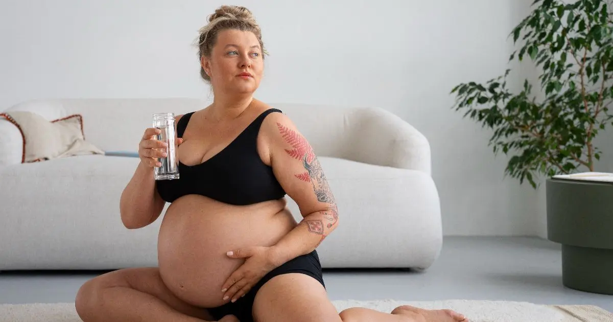 Pregnancy After 40: It’s Not Too Late — Just a Different Kind of Challenge Pregnancy After 40 featuring a confident pregnant woman sitting at home, holding a glass of water and embracing her body.
