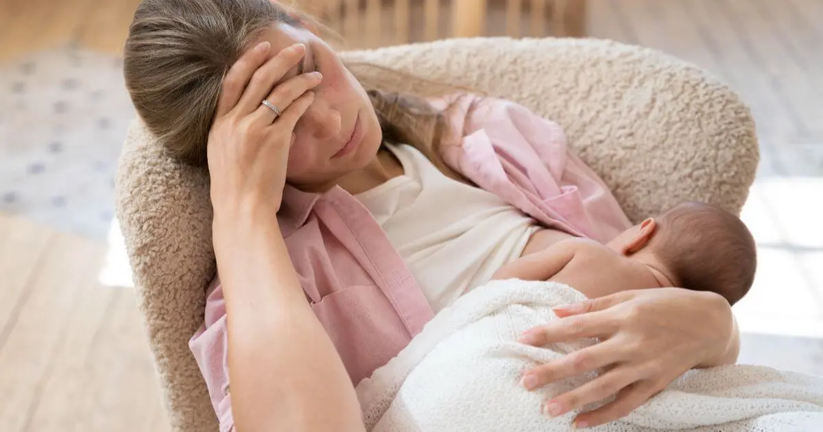 Tired mother breastfeeding her baby while showing signs of Mom Burnout in Summer, highlighting exhaustion, mental overload, and the challenges of caring for a newborn during the summer months.