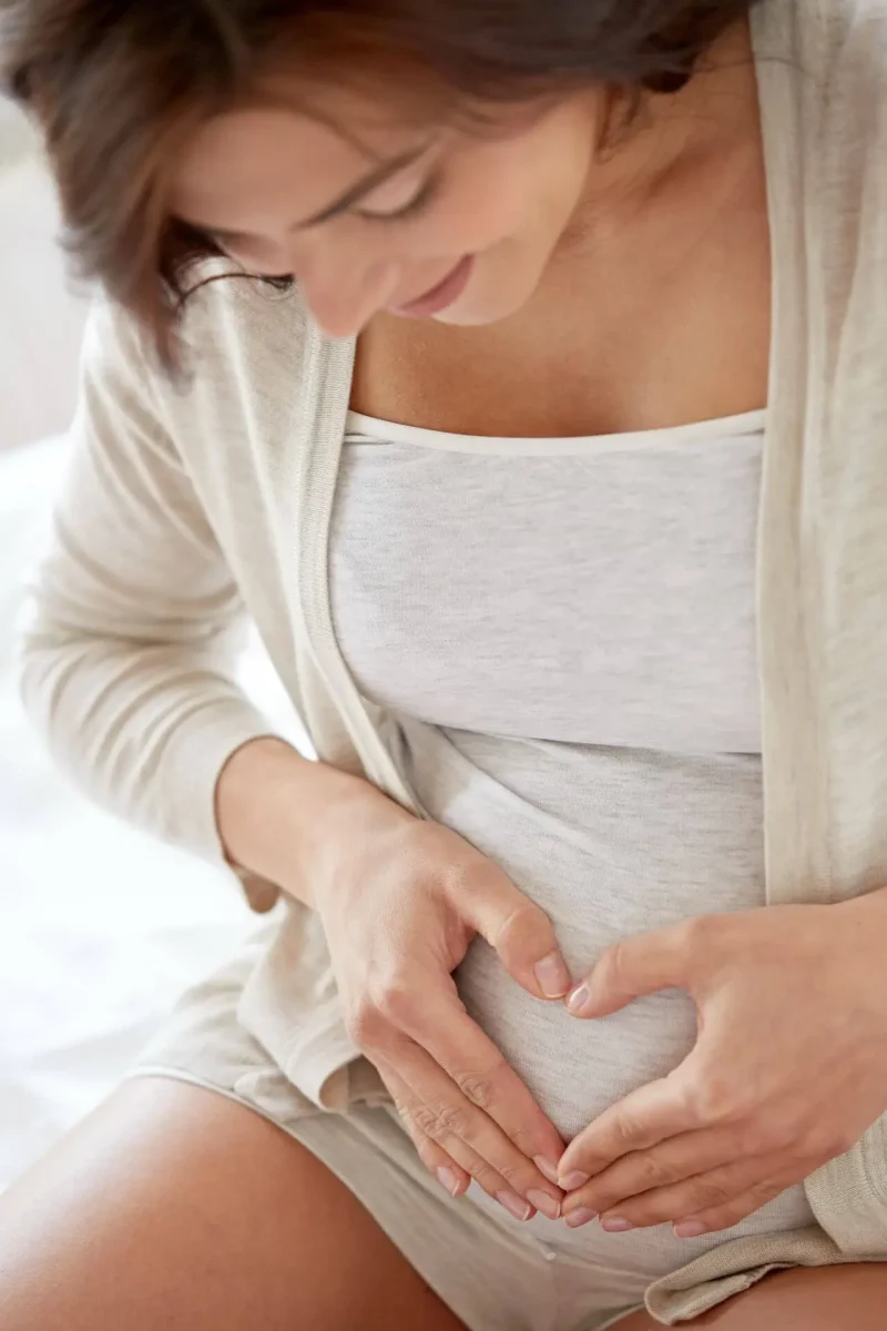 Pregnant woman gently holding her baby bump in a heart shape while paying attention to early labor contractions and the emotional final weeks before childbirth.