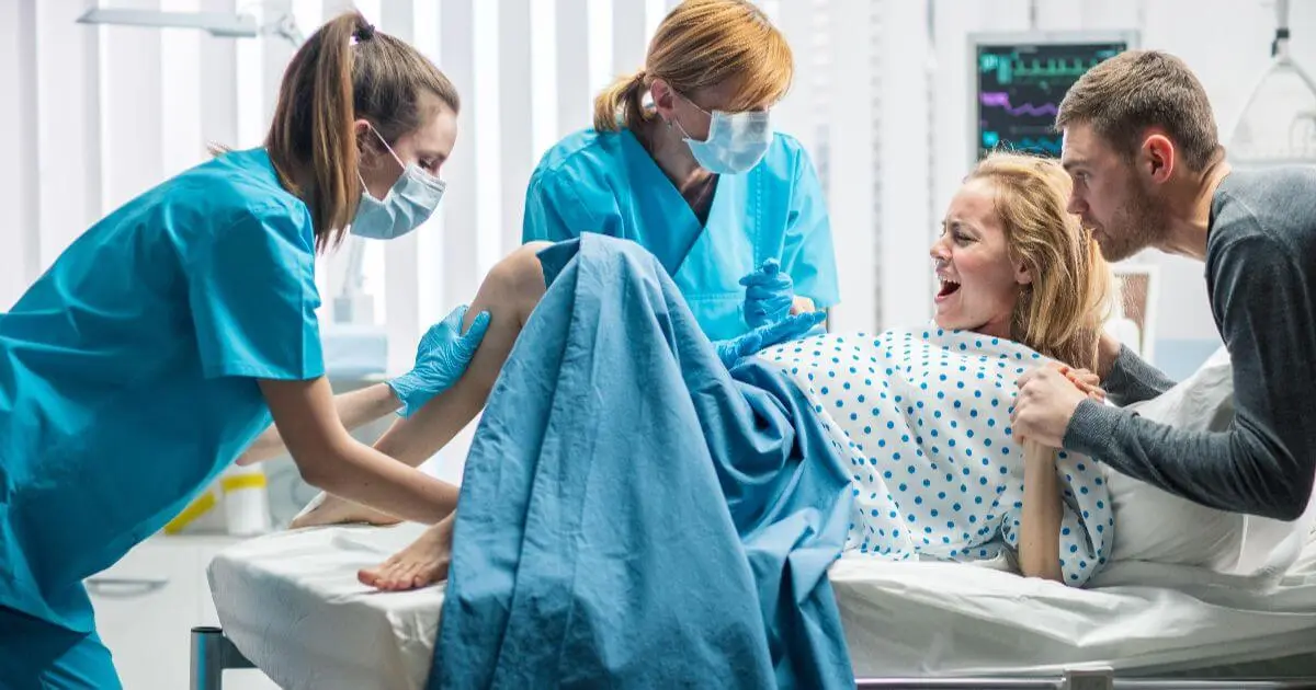 The Stages of Labor: What Really Happens During Labor and Birth? Stages of Labor photo showing a mother in active labor during childbirth, supported by medical staff and her partner in a hospital delivery room.