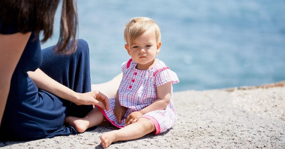 Mom Burnout in Summer: Mother sitting by the water with her toddler, balancing childcare responsibilities, emotional demands, and the daily challenges of motherhood during the summer months.