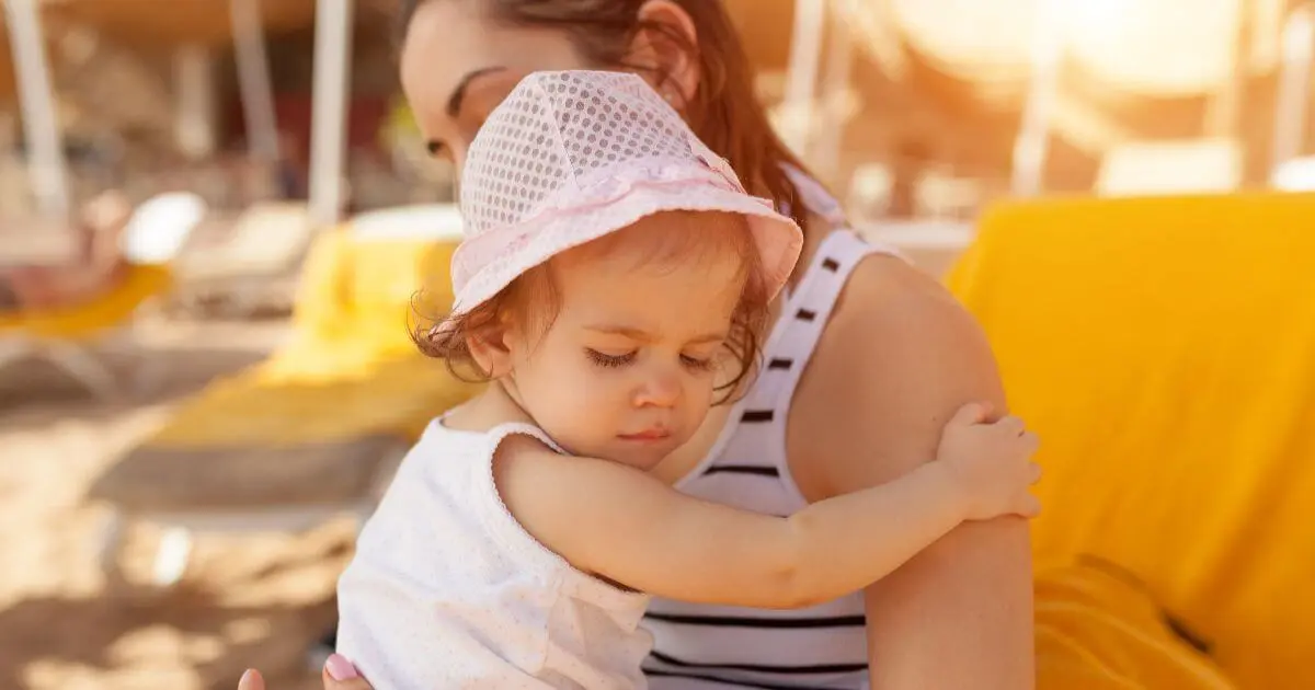 Mom Burnout in Summer: Mother holding a tired toddler during a family vacation, highlighting the exhaustion, mental load, and parenting challenges that often continue even while everyone else is on vacation.