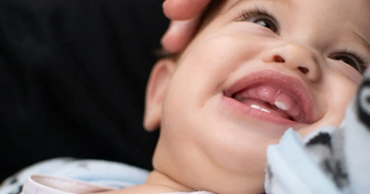 Baby teething smiling infant with visible new tooth breaking through gums