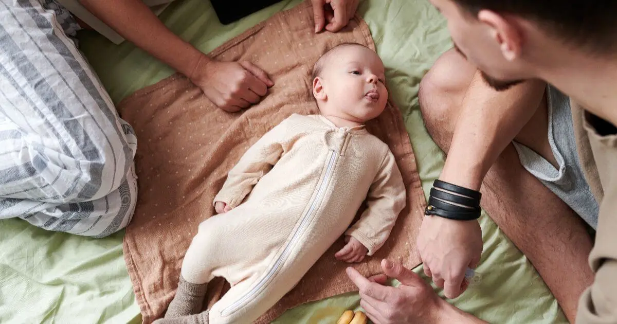 Baby wearing a modern swaddling sleep sack while parents watch nearby, highlighting a safe and easy swaddling alternative for newborn sleep routines.