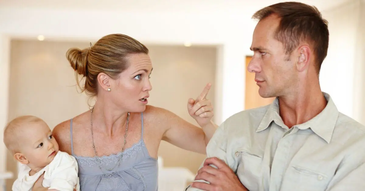 mother pointing at father while holding baby during argument, conflict and frustration in relationship after baby
