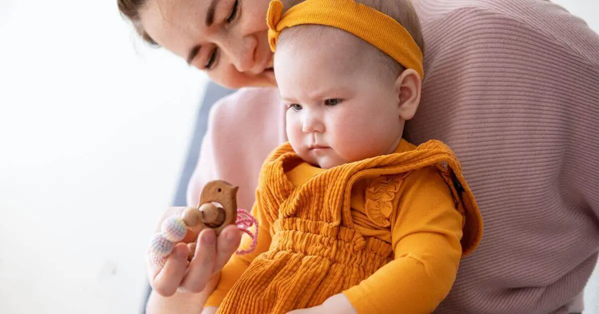 What to Play With Your Baby (3–12 Months): Simple Developmental Activities What to Play With Your Baby: mom carrying baby girl while she plays with teething beads.