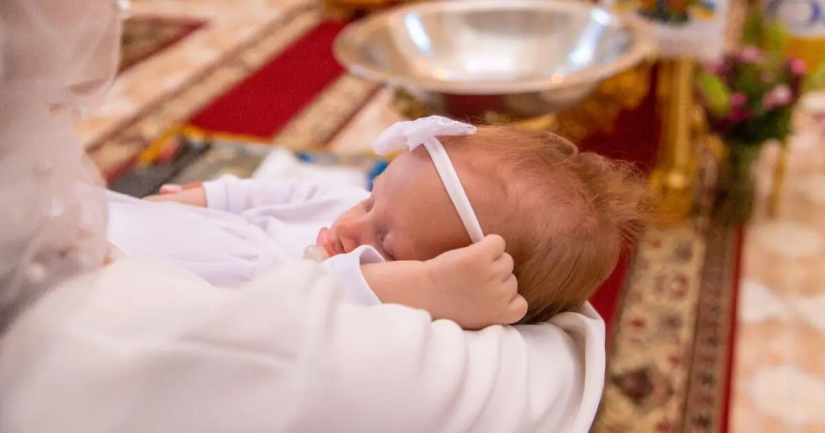 Sleeping baby in white outfit during Baptism, held gently in church setting