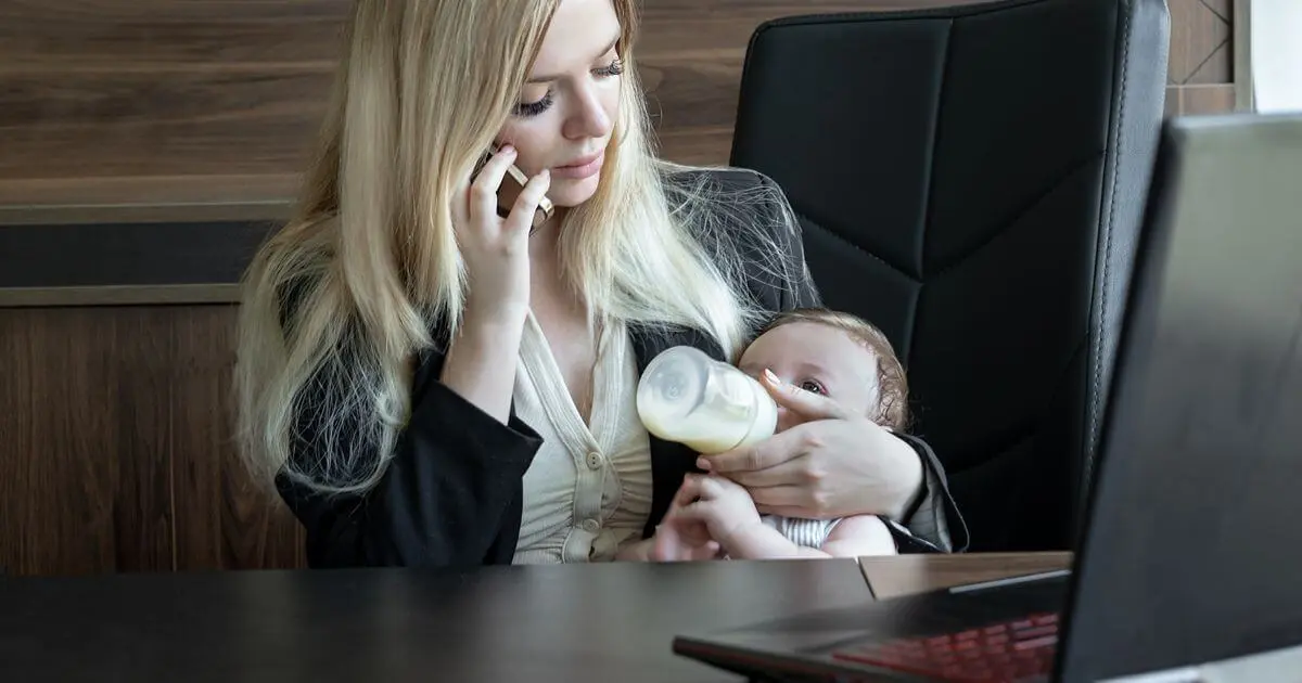 Returning to Work: Mom feeding her baby with a bottle while handling a work phone call at the office after maternity leave.