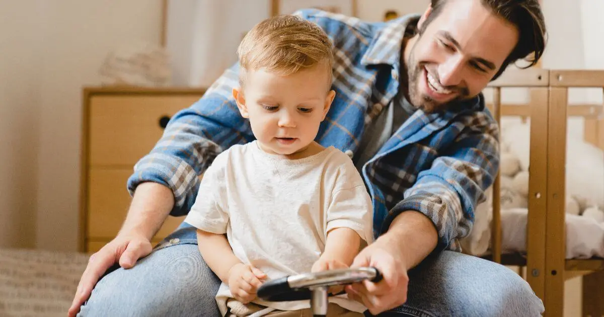 The Simplest Way to Become the Father Your Child Will Never Forget Father helping his toddler play with a toy car at home, showing supportive parenting, child development activities, and strong father-child bonding moments.