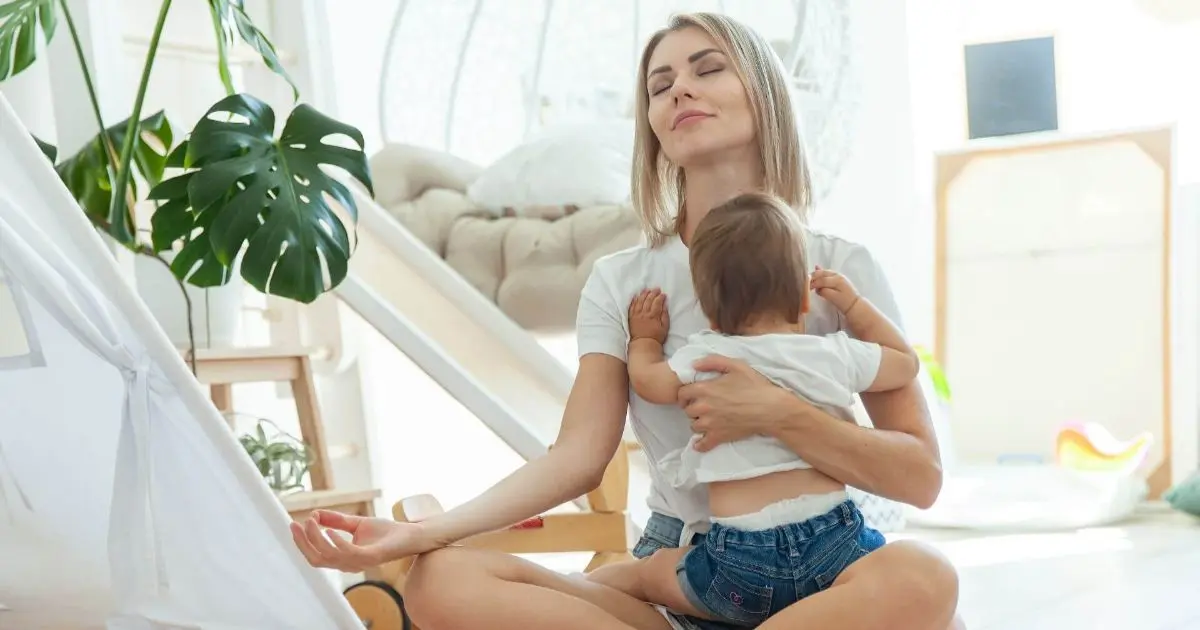 Mom burnout recovery — young mother meditating at home while spending calm, mindful time with her baby, representing stress relief and emotional balance.