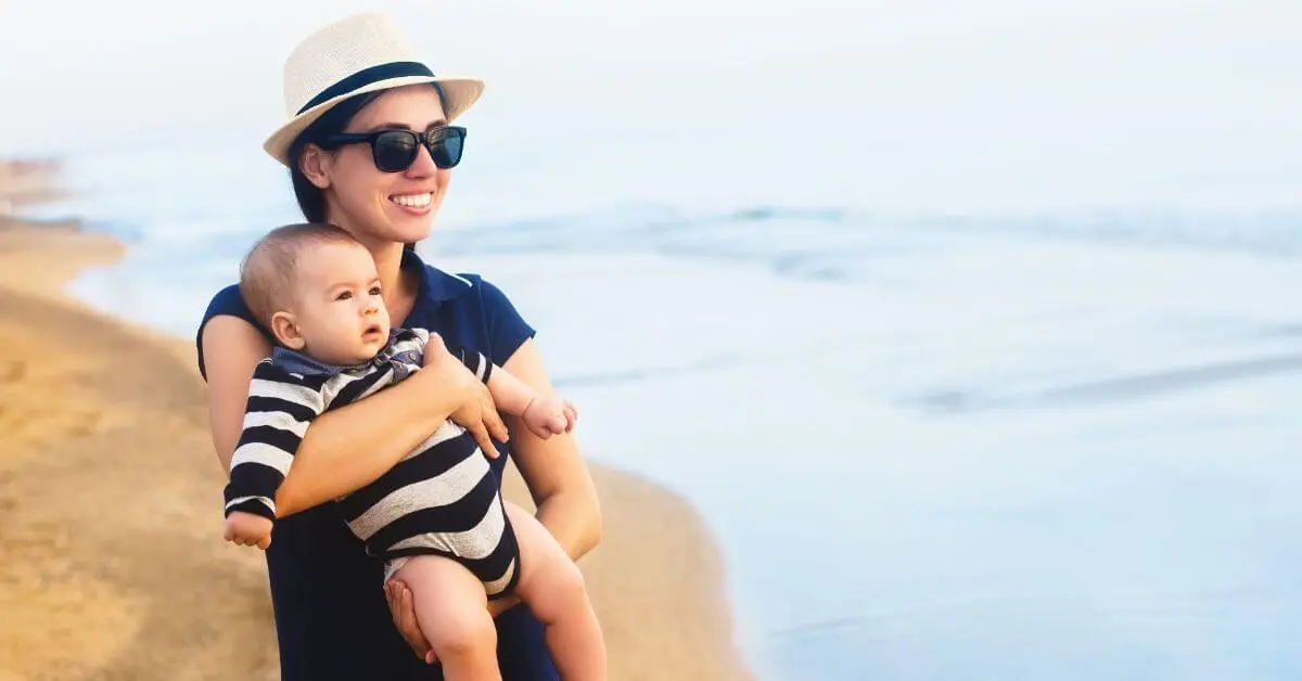 Young mother walking with her baby boy on the beach while vacationing with a baby