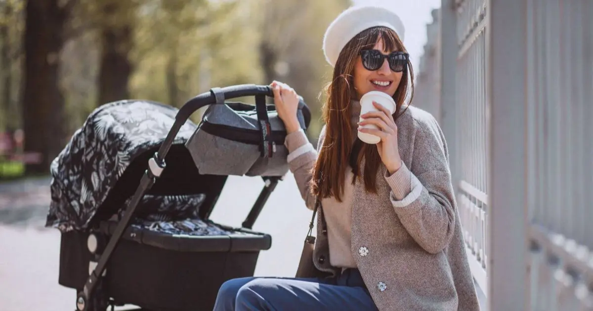 Diaper bag tips: young mother walking with a baby carriage in a park, enjoying a calm everyday moment while out with her baby.