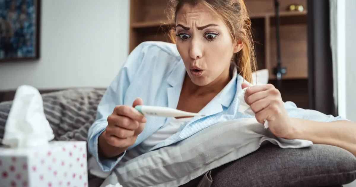 Early Pregnancy Symptoms: a worried woman lying on a couch looking at a thermometer, feeling unwell as a possible early pregnancy sign.